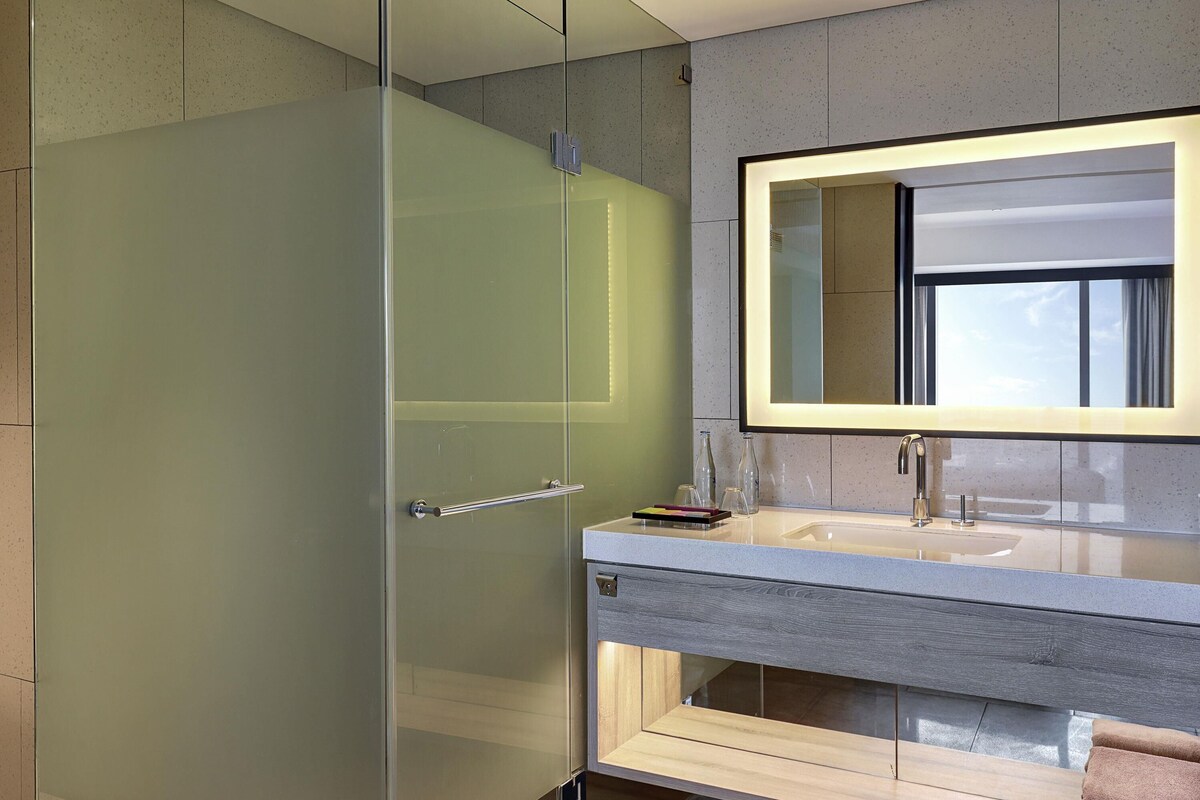 Une salle de bain moderne avec une douche à l’italienne en verre, un grand miroir et un meuble-lavabo en bois.