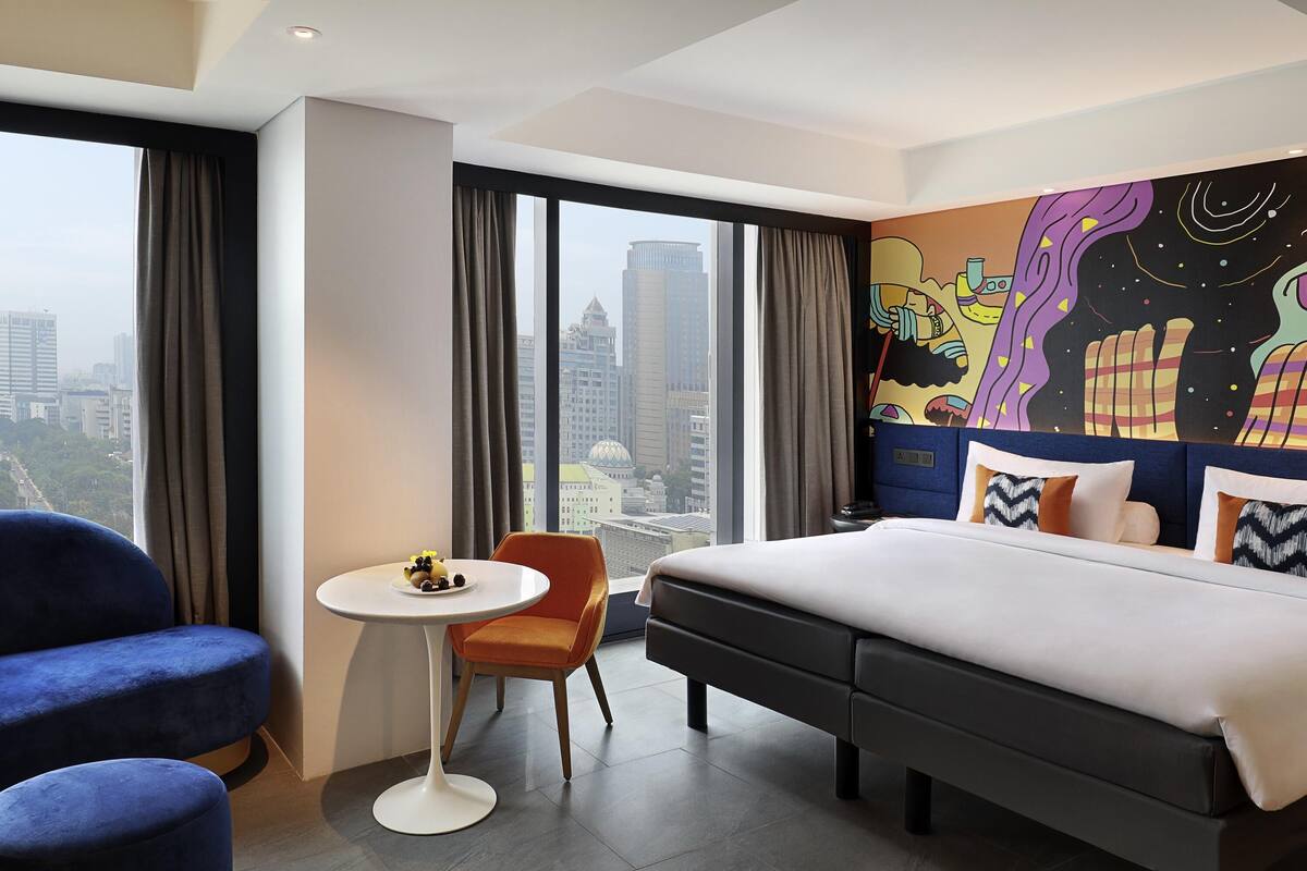 Habitación de hotel con una cama grande, una mesa redonda pequeña, dos sillas y vista a la ciudad.