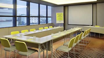 A conference room with a long table, yellow chairs, a projector screen, and a window with a city view.