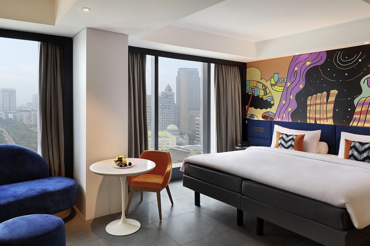 Une chambre d’hôtel avec un grand lit, une petite table ronde, deux chaises et une vue sur la ville.