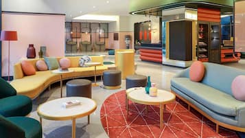 A modern lounge area with sofas, round tables, and a red patterned rug.