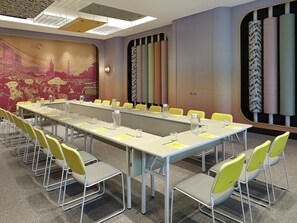 Une salle de conférence avec une longue table, des chaises jaunes et un mur orné de motifs.