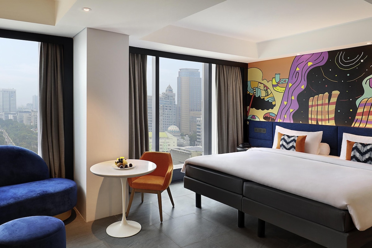 Een hotelkamer met een groot bed, een klein rond tafeltje, twee stoelen en uitzicht op de stad.