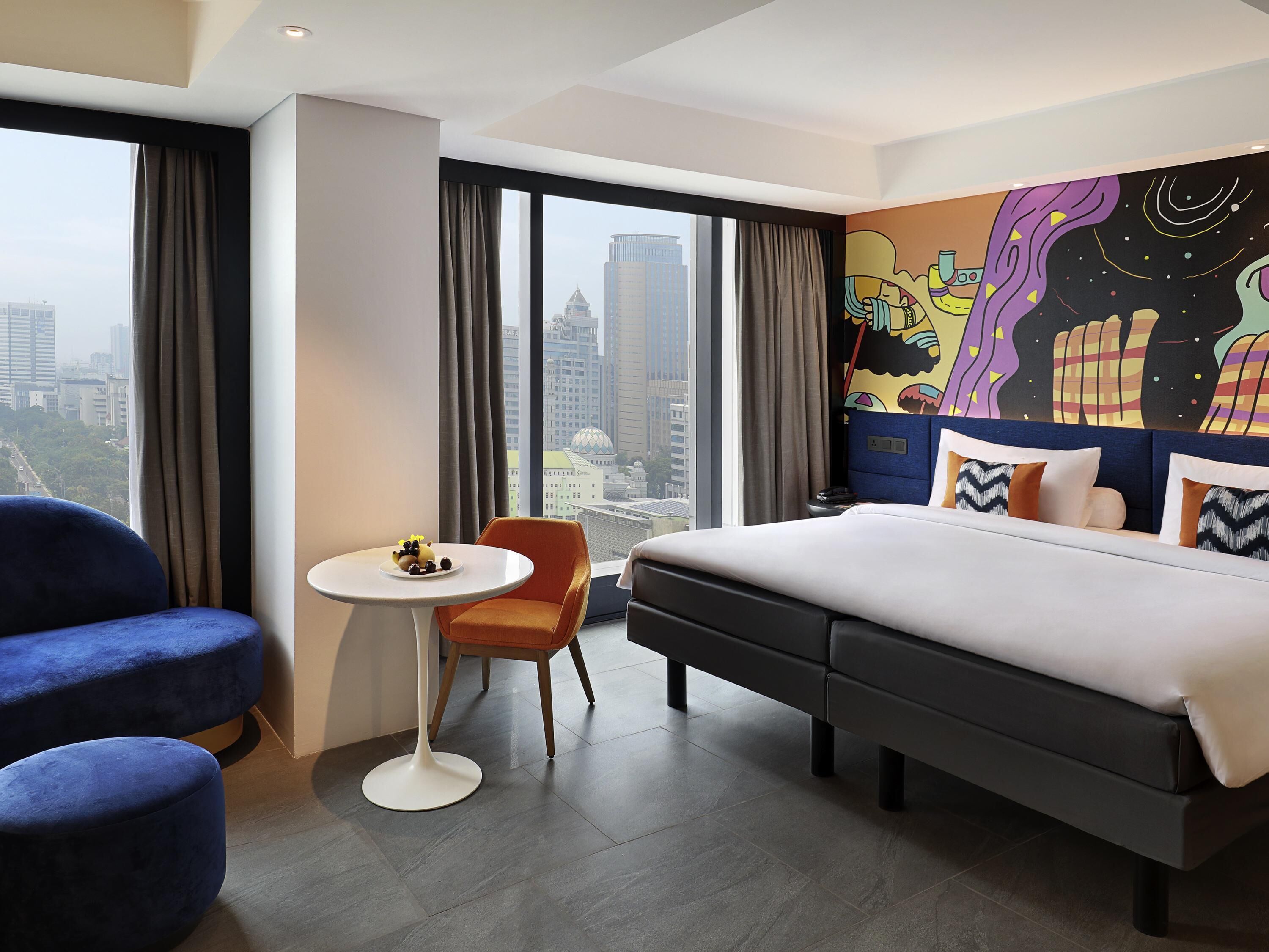 Habitación de hotel con una cama grande, una mesa redonda pequeña, dos sillas y vista a la ciudad.