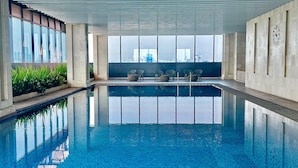 Ein moderner, überdachter Pool mit klarem, blauen Wasser, großen Fenstern und Sitzbereichen.