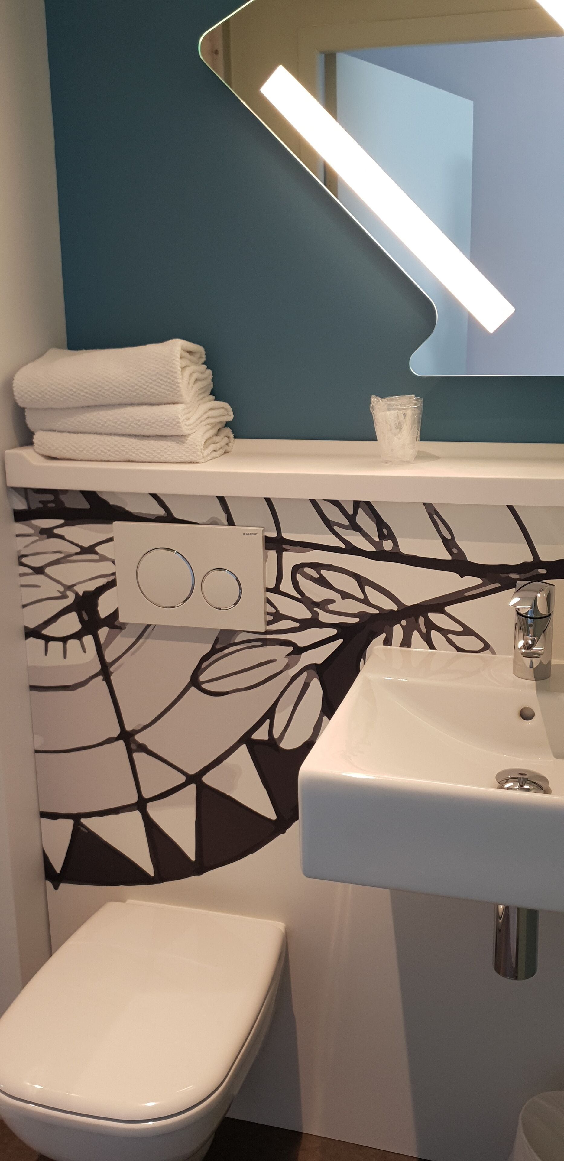 A bathroom with a white toilet, a sink with a mirror above it, and a towel rack with folded towels.