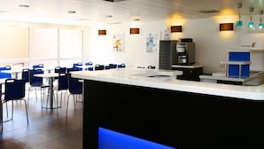 A modern cafe with a central counter, blue chairs, and a coffee machine. - ibis budget Aubenas (Aubenas)