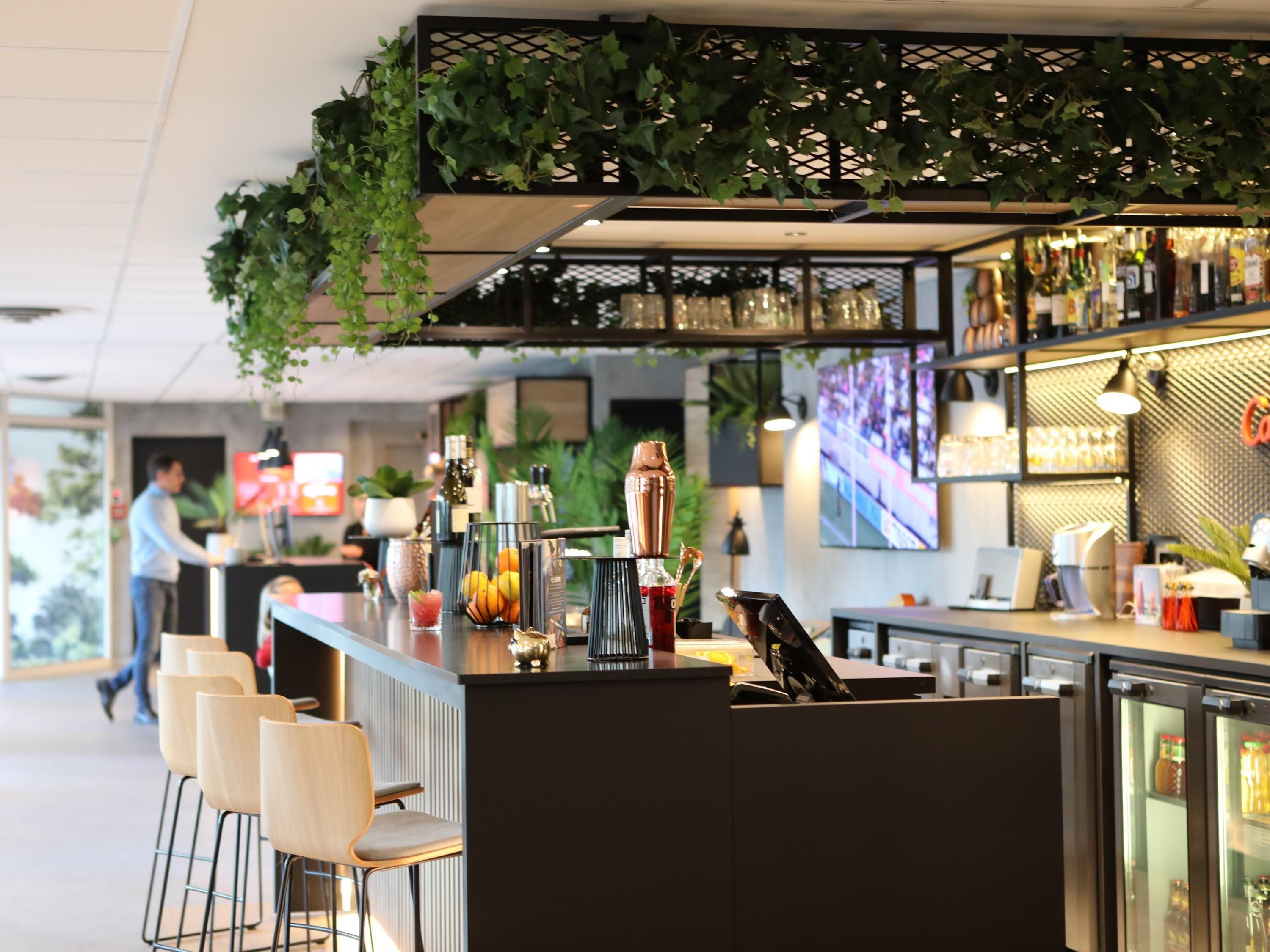 A bar area with seating, a counter with bar tools, and a decorative ceiling with hanging plants.