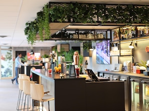 Een bar met zitplaatsen, een toonbank met bar gereedschap en een decoratief plafond met hangende planten.
