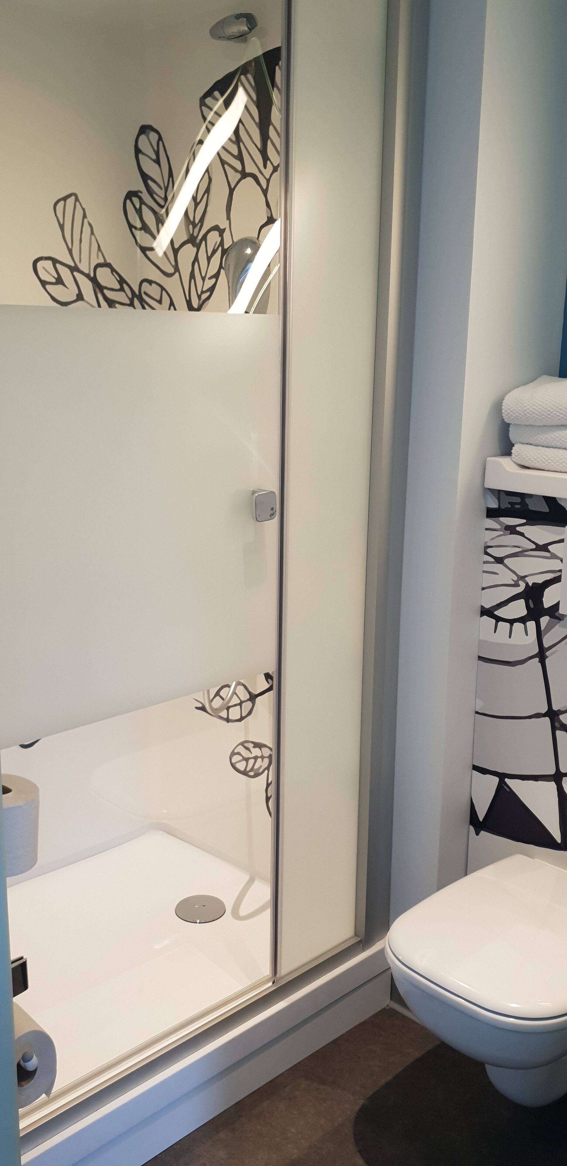 Un baño con cabina de ducha de vidrio, inodoro y perchero para toallas.