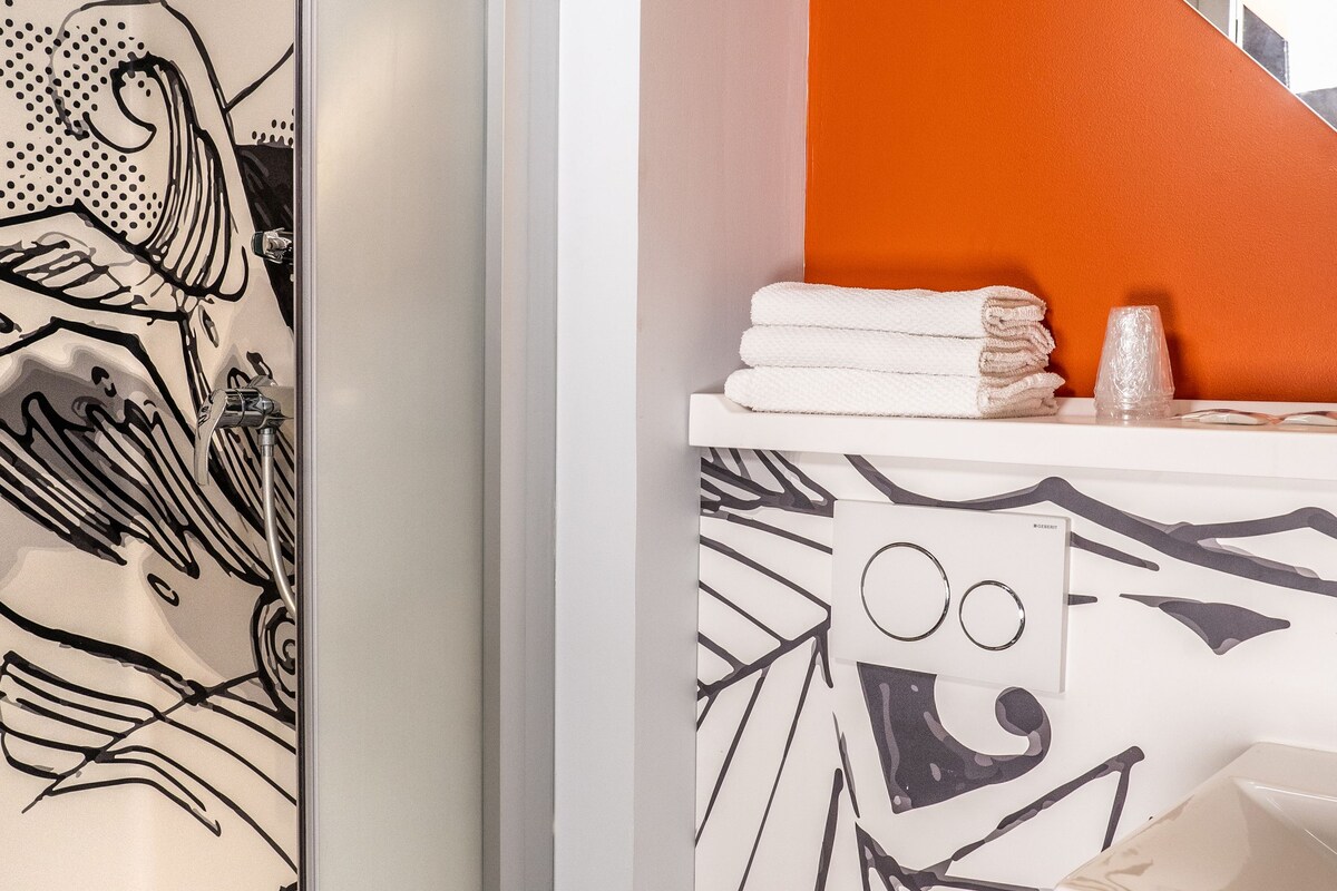 Une salle de bain dotée d’une douche à parois de verre, de toilettes et d’un lavabo, le tout agrémenté d’un motif géométrique sur le mur.