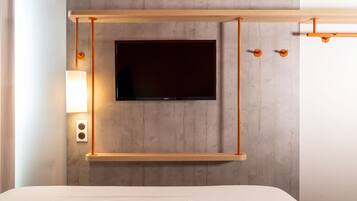 Una habitación de hotel moderna con un televisor montado, repisa de madera y lámpara de pared.