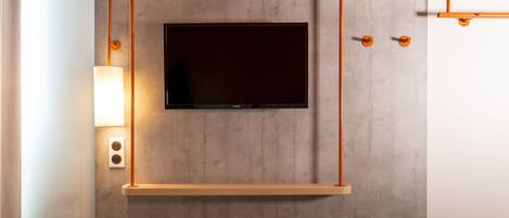 Una habitación de hotel moderna con un televisor montado, repisa de madera y lámpara de pared.