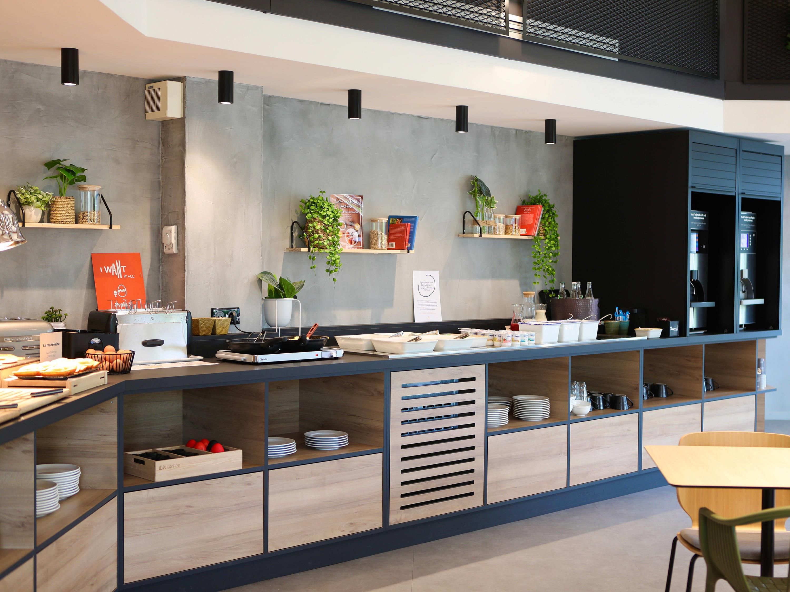Une cuisine moderne dotée d’un long comptoir, de divers appareils électroménagers et d’étagères où sont disposées des plantes et des ustensiles de cuisine.