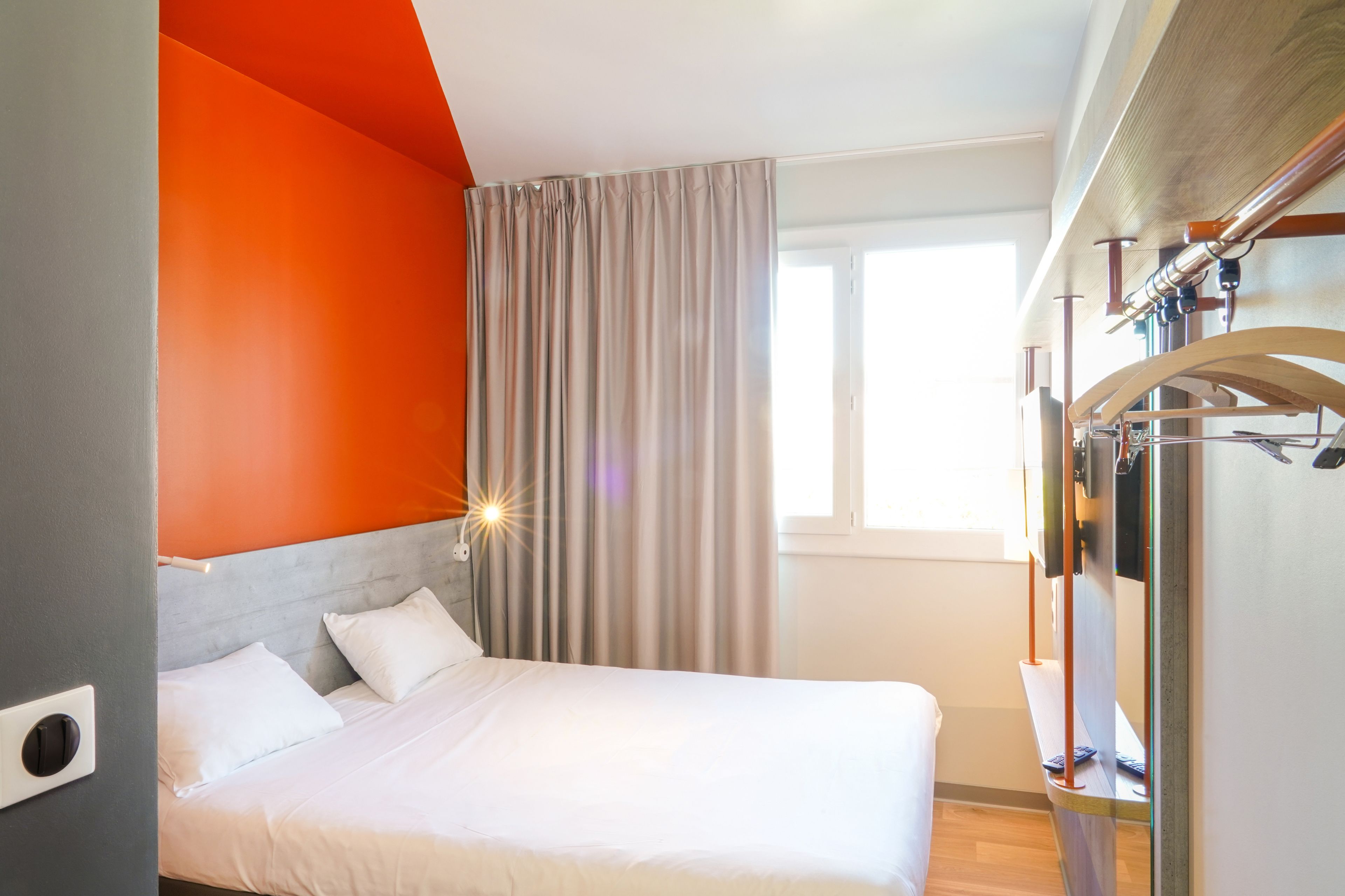A modern hotel room with a bed, a window with curtains, and a wooden ceiling.