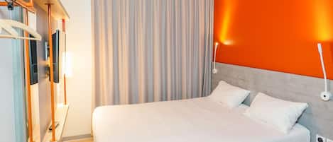 Una habitación de hotel moderna con una cama grande, televisión, escritorio con silla y cortina.