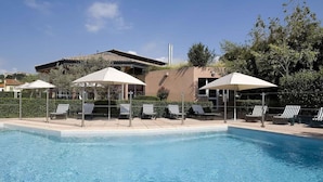 A swimming pool with lounge chairs and umbrellas, surrounded by greenery and a building with a tiled roof. - ibis budget Aubenas (Aubenas)