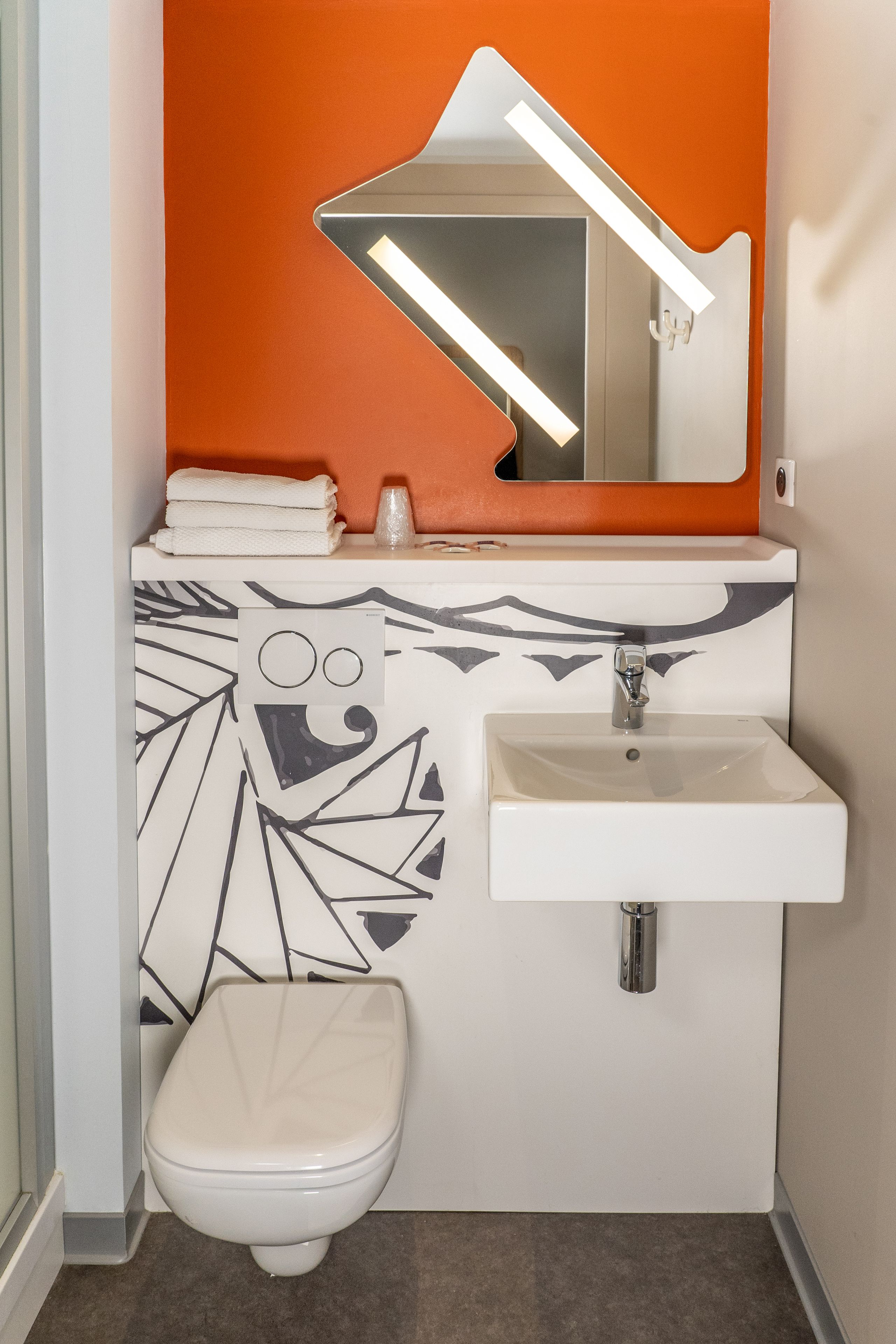 Un baño con lavamanos blanco, inodoro y pared de acento naranja.