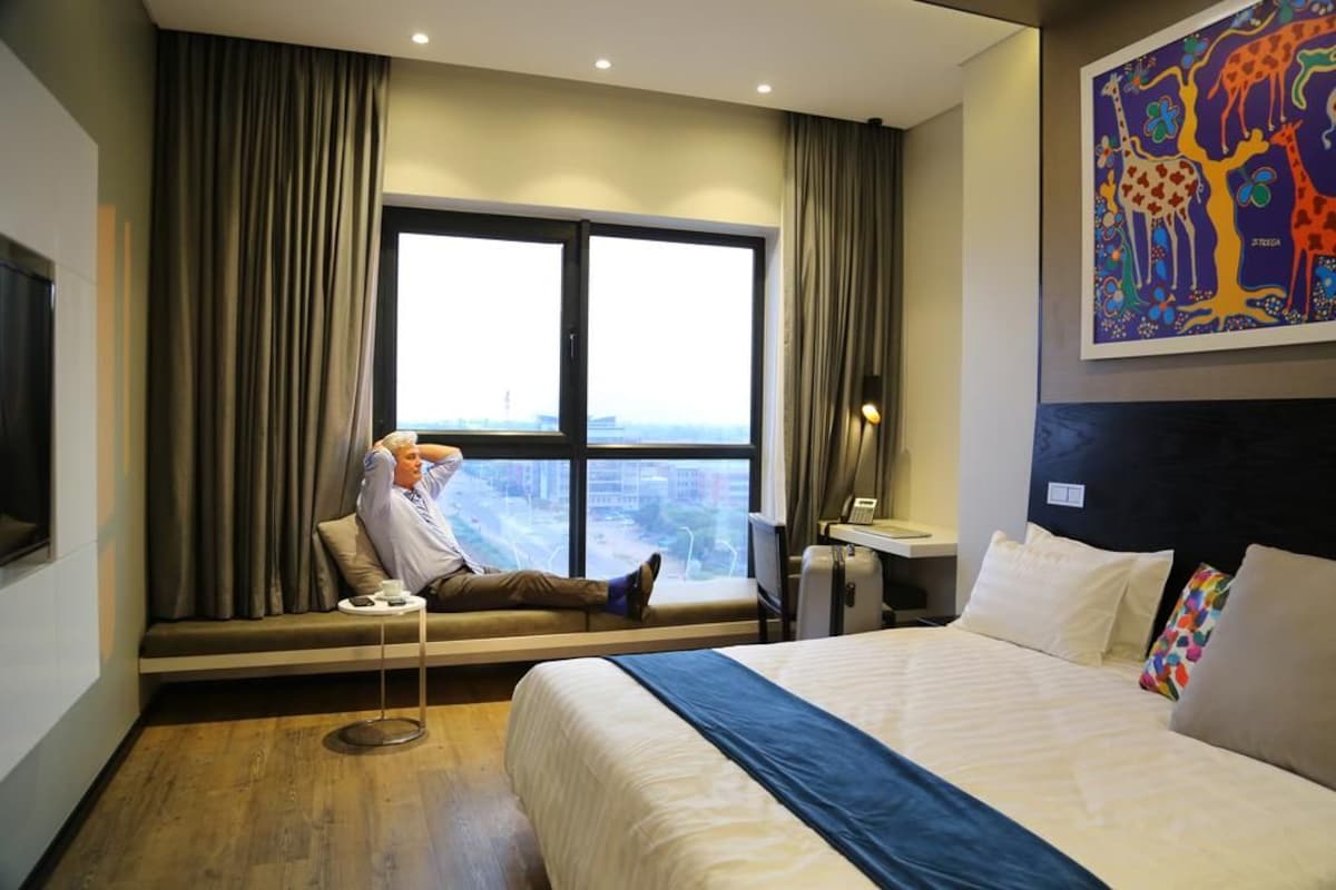 Habitación de hotel con cama, ventana con cortinas, escritorio y un cuadro en la pared.