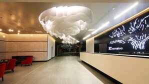 Eine moderne Lobby mit einem einzigartigen Deckenstil, einem Empfangsbereich und roten Sitzgelegenheiten.