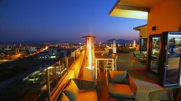 A rooftop terrace with a city view, a table with chairs, and a lounge area.