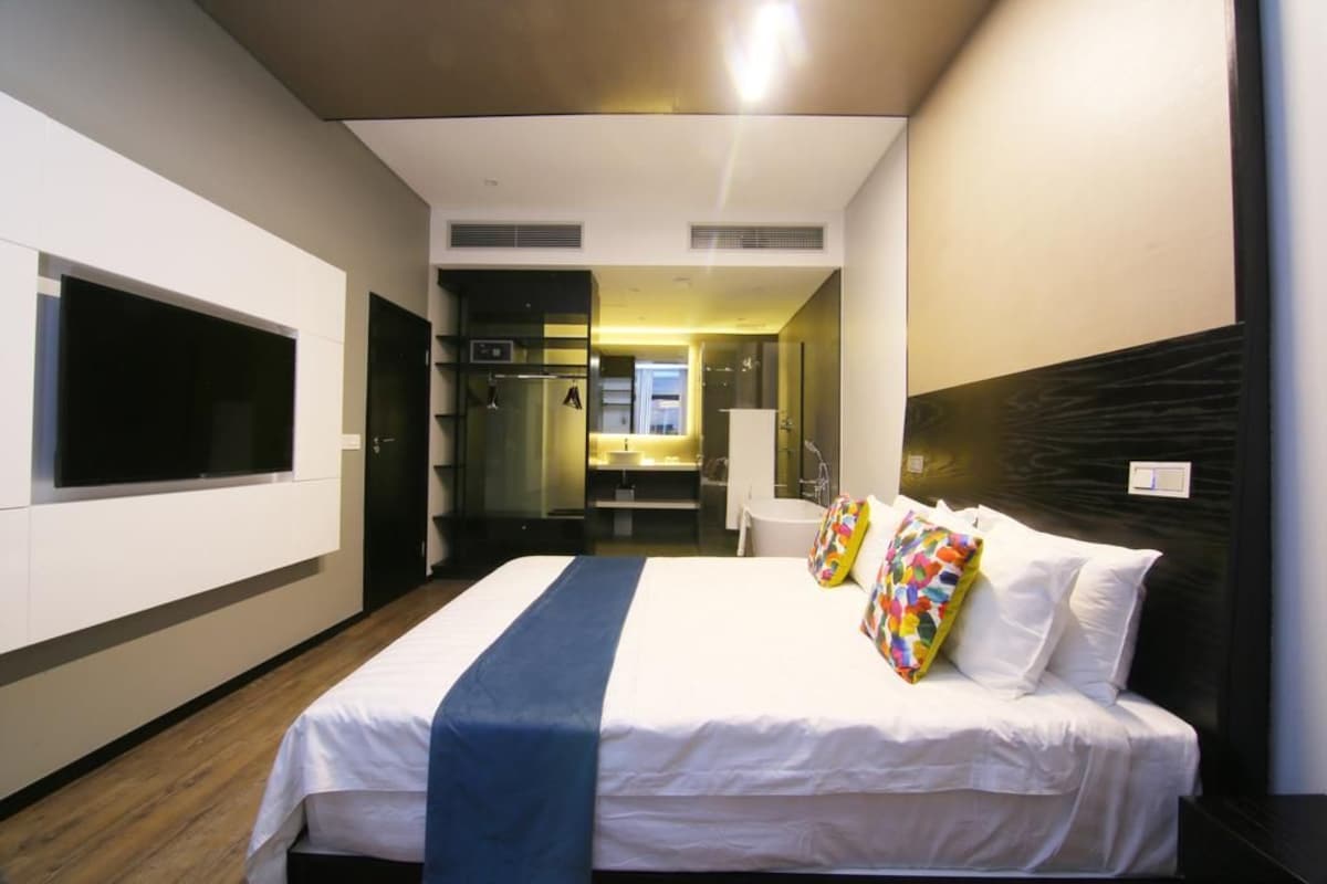 Una habitación de hotel moderna con una cama grande, televisión, baño y vistas a la ciudad.