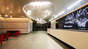 A modern lobby with a unique ceiling design, a reception desk, and red seating. - Room50two (Gaborone)