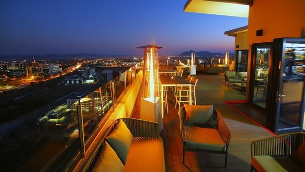 Eine Dachterrasse mit Blick auf die Stadt, ein Tisch mit Stühlen und eine Lounge-Ecke.