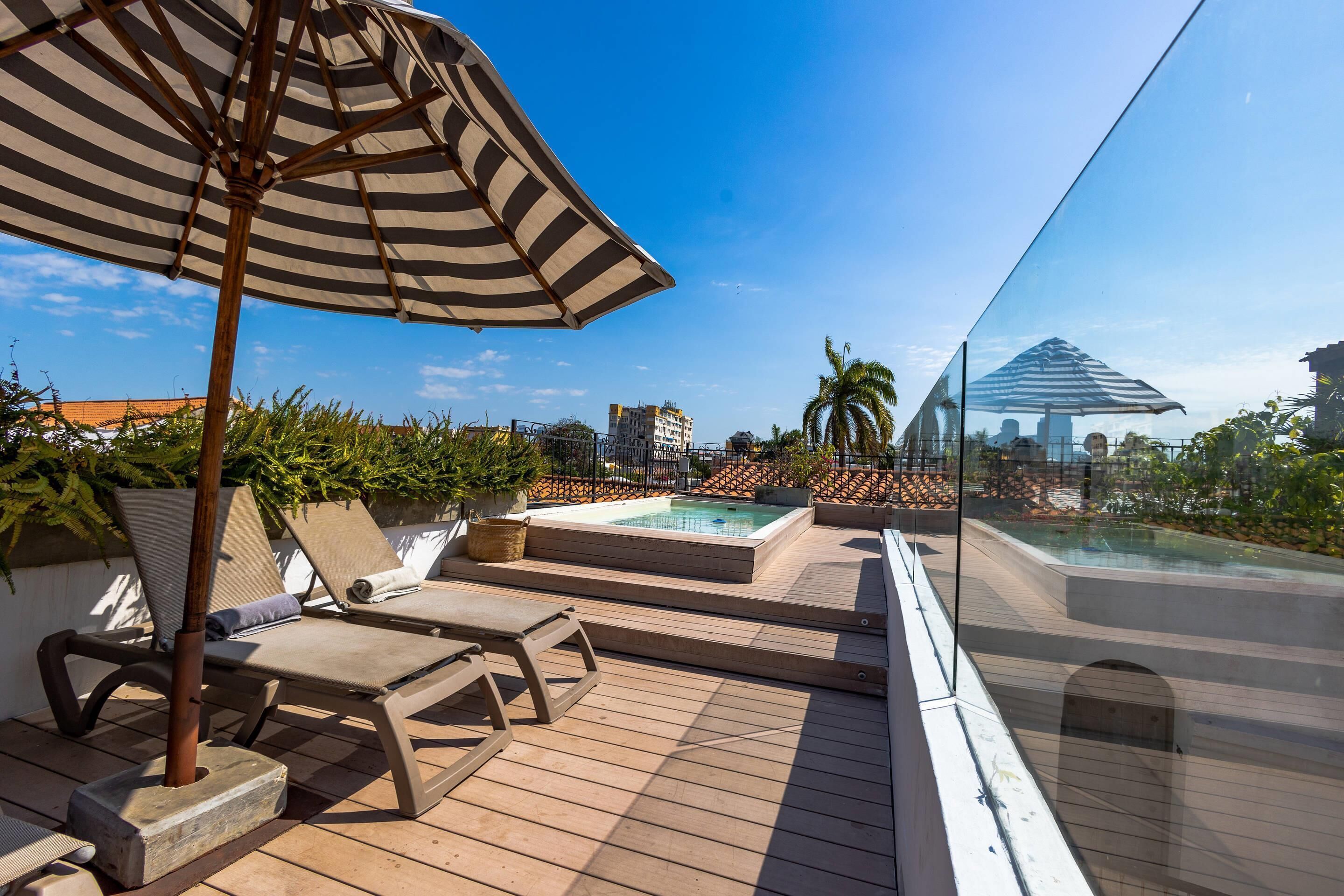 A rooftop deck with lounge chairs, a hot tub, and a glass balustrade overlooking a cityscape.