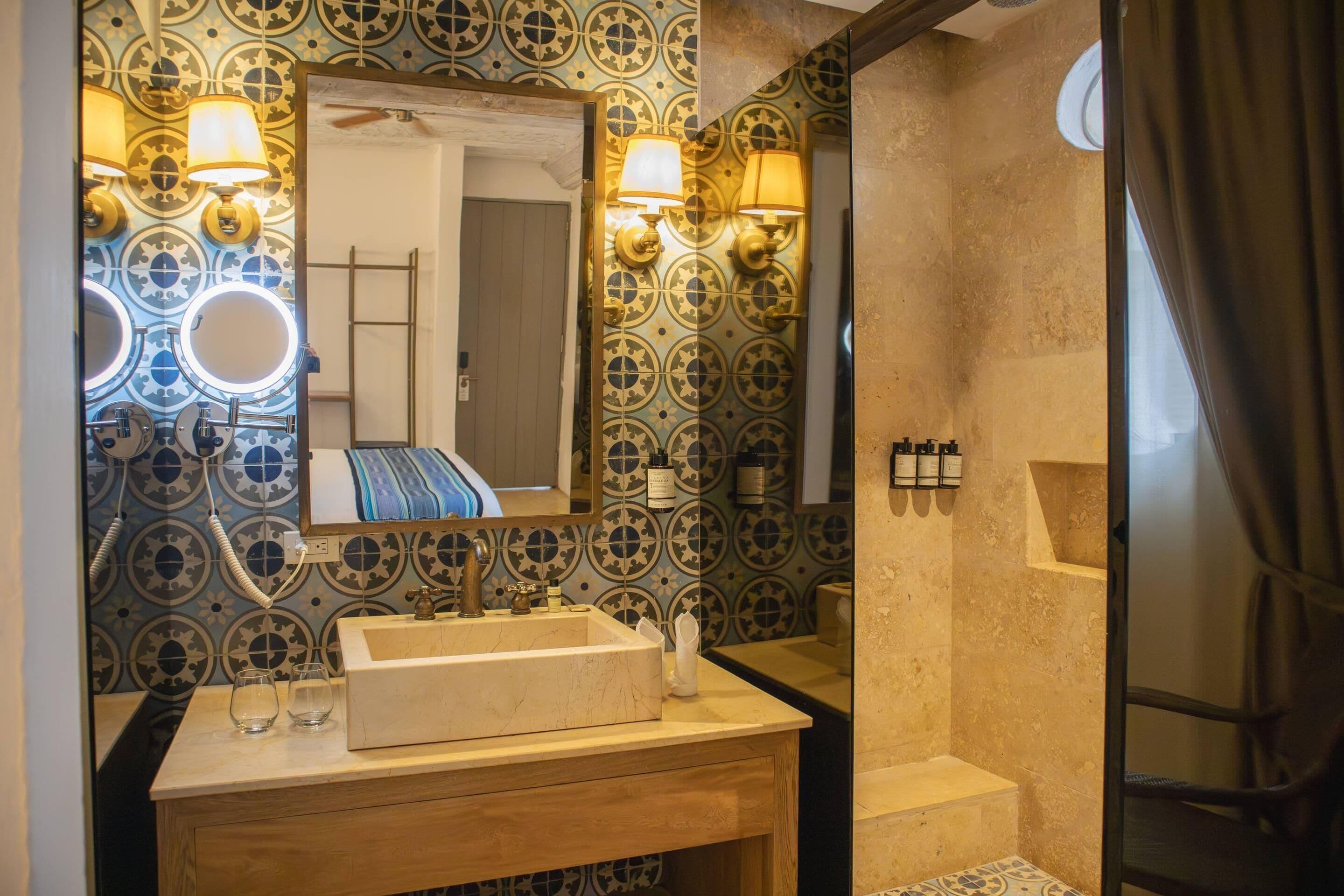 A bathroom with a sink, mirror, and patterned wall tiles.
