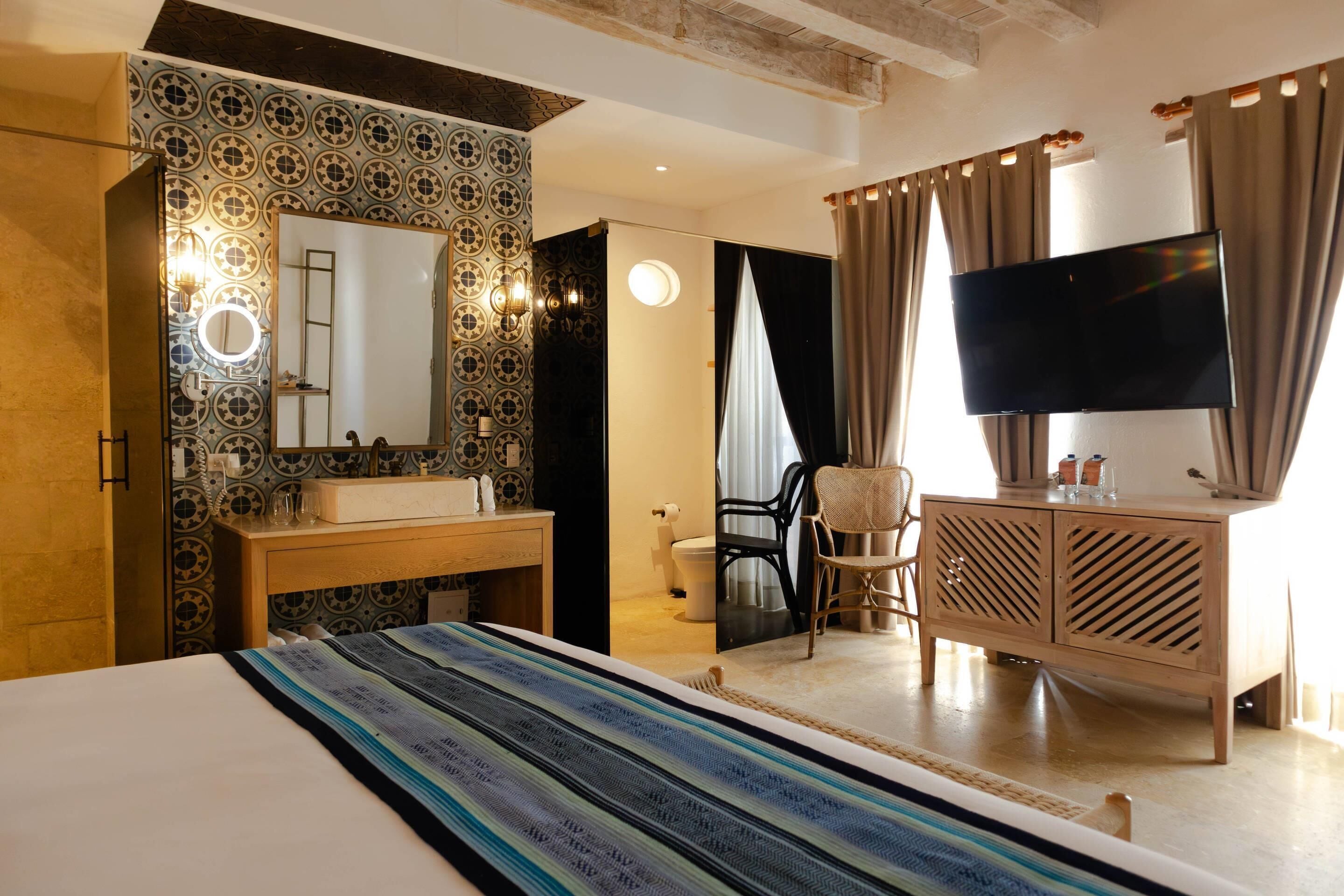 A hotel room with a bed, a vanity with a mirror, a television, a desk, and a chair.