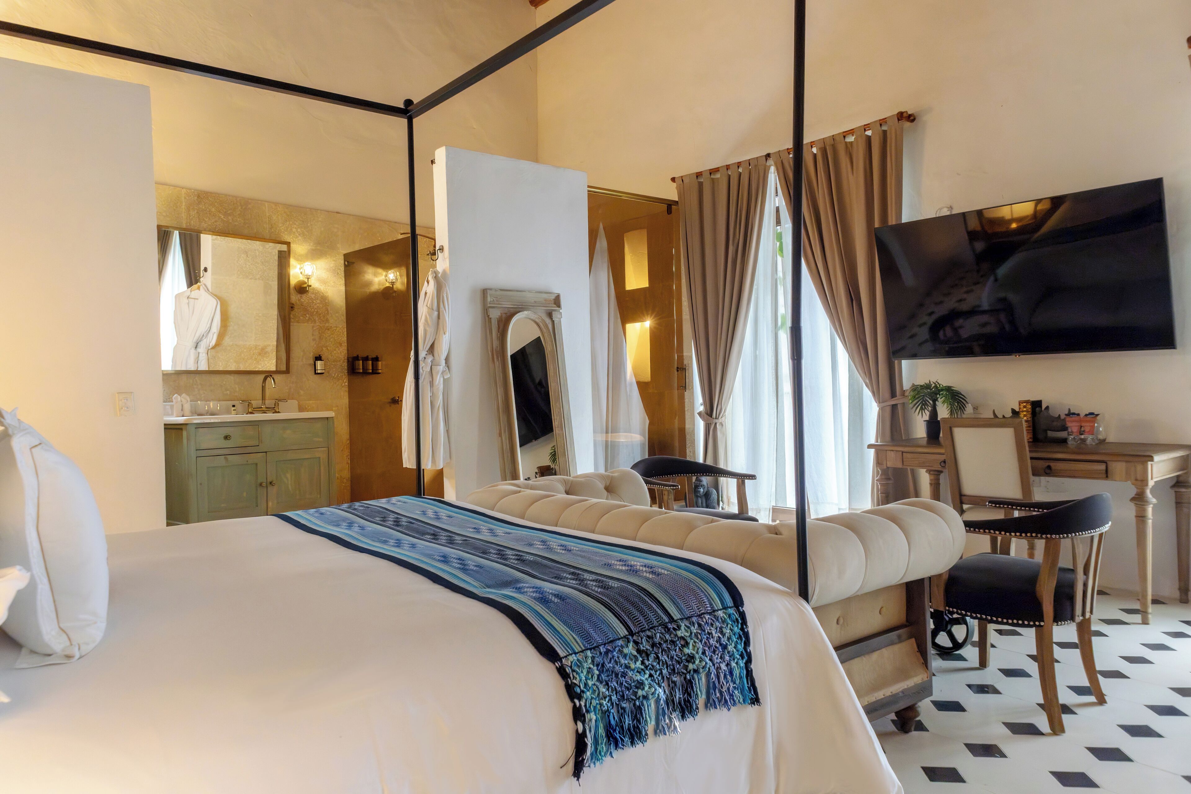 Ein Schlafzimmer mit einem großen Bett, einem Schreibtisch, einem Stuhl, einem Fernseher und einem Badezimmer mit Spiegel und Waschbecken.