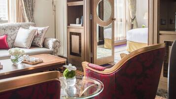 A hotel room with a sofa, armchairs, a glass coffee table, a bed, and a wardrobe.