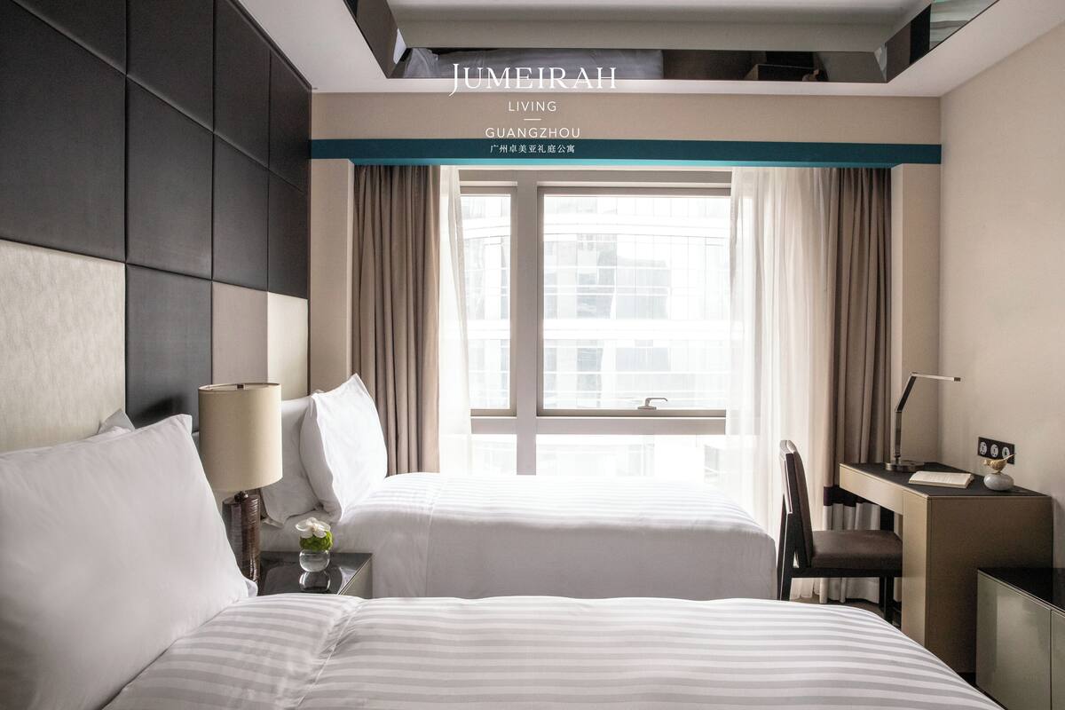 Una habitació d'hotel amb dos llits, un escriptori i una finestra amb cortines.