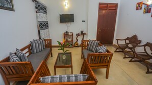 A living room with wooden furniture, a flat-screen TV, a decorative wall hanging, and a wooden door. - Saku Residence (Unawatuna)
