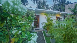 A modern building with a pathway leading to the entrance, surrounded by lush greenery and palm trees. - Saku Residence (Unawatuna)