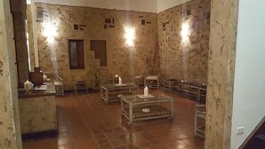 A room with rustic walls, a wooden floor, and a central glass table with candles. There are chairs and a small table with a vase. - Hotel Refugio del Inca (Salta)
