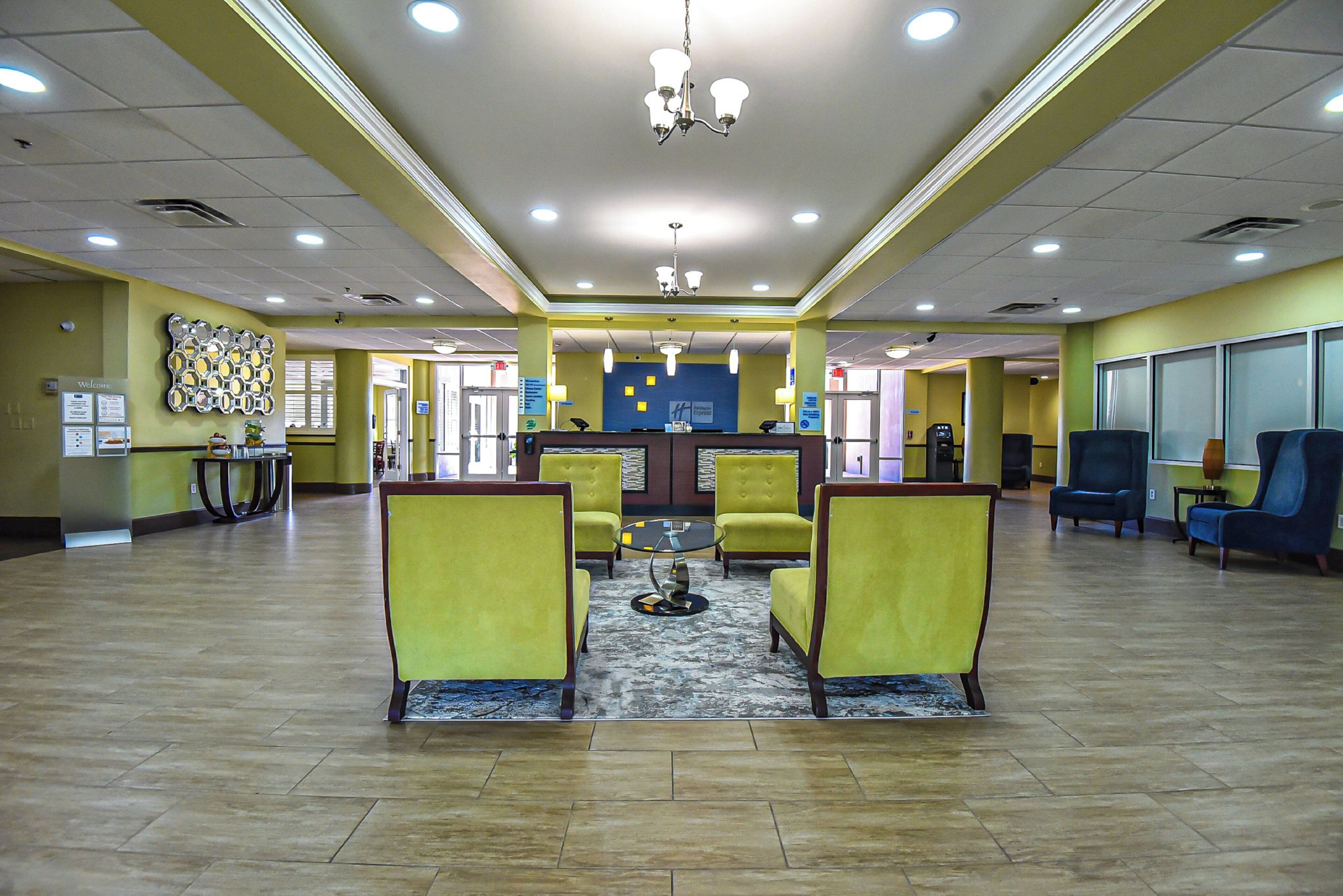A lobby with a reception desk, yellow chairs, a patterned rug, and a chandelier.