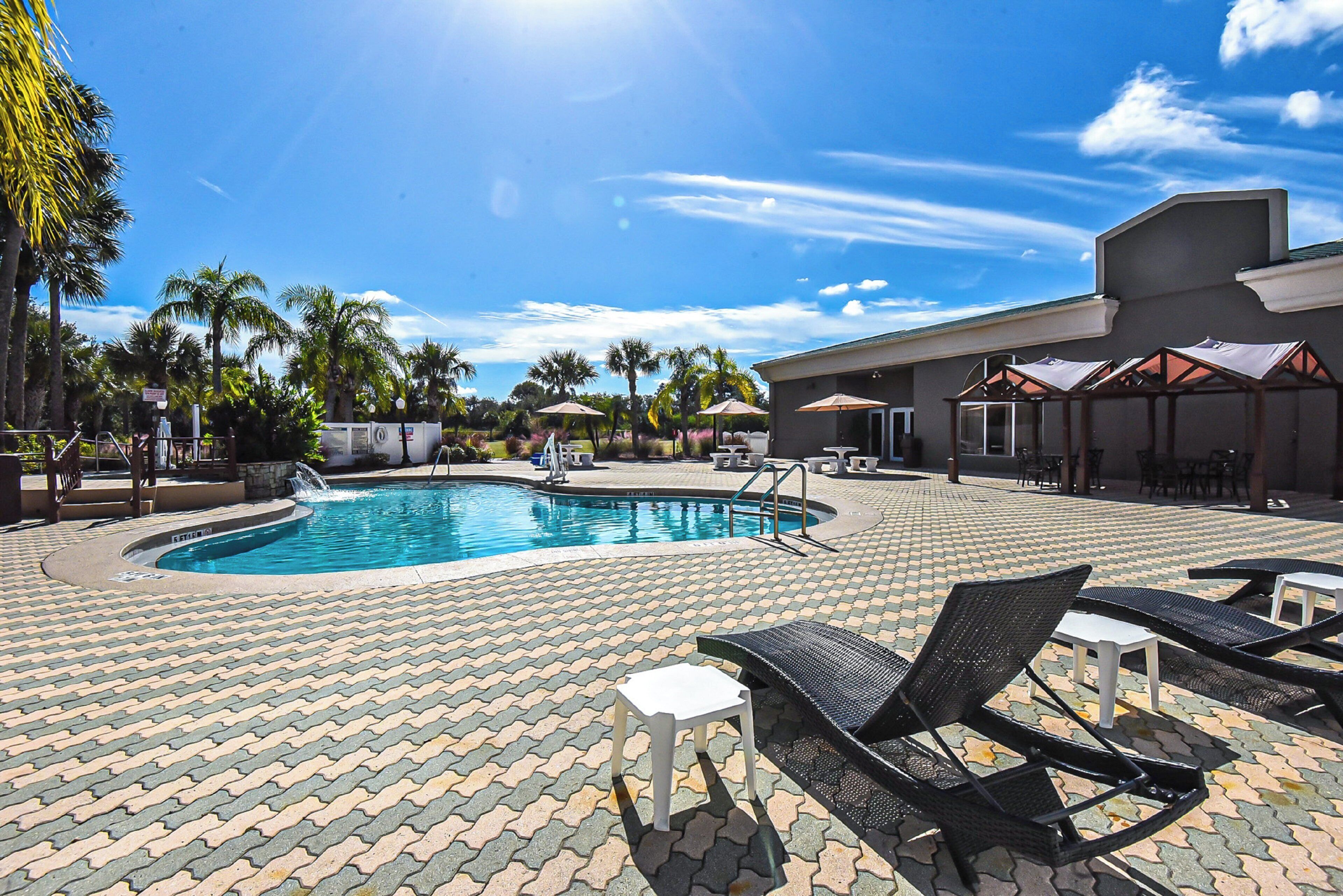 A swimming pool with lounge chairs and umbrellas, surrounded by palm trees and a tiled patio.