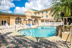 A hotel with a swimming pool, lounge chairs, and a palm tree.