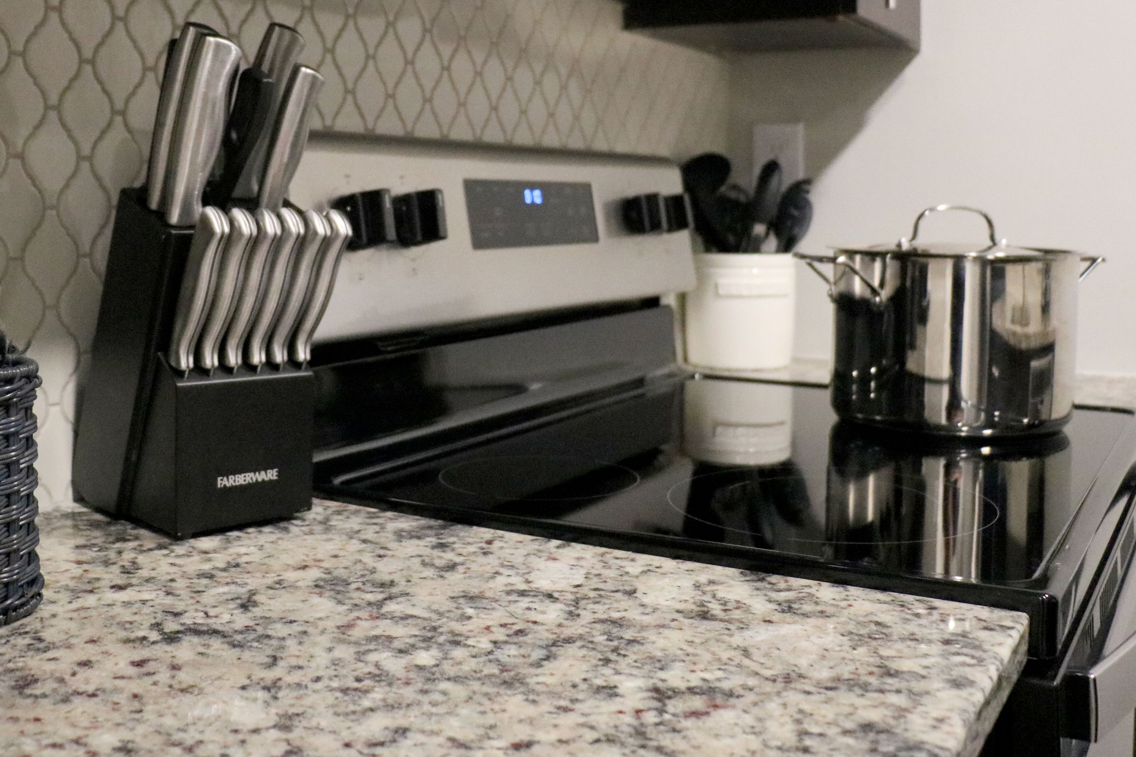 A kitchen with a granite countertop, a stove, a pot, and a knife holder.