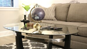 A living room with a glass coffee table, a globe, and a remote control. - Remarkable One Bedroom Suite (Boston)