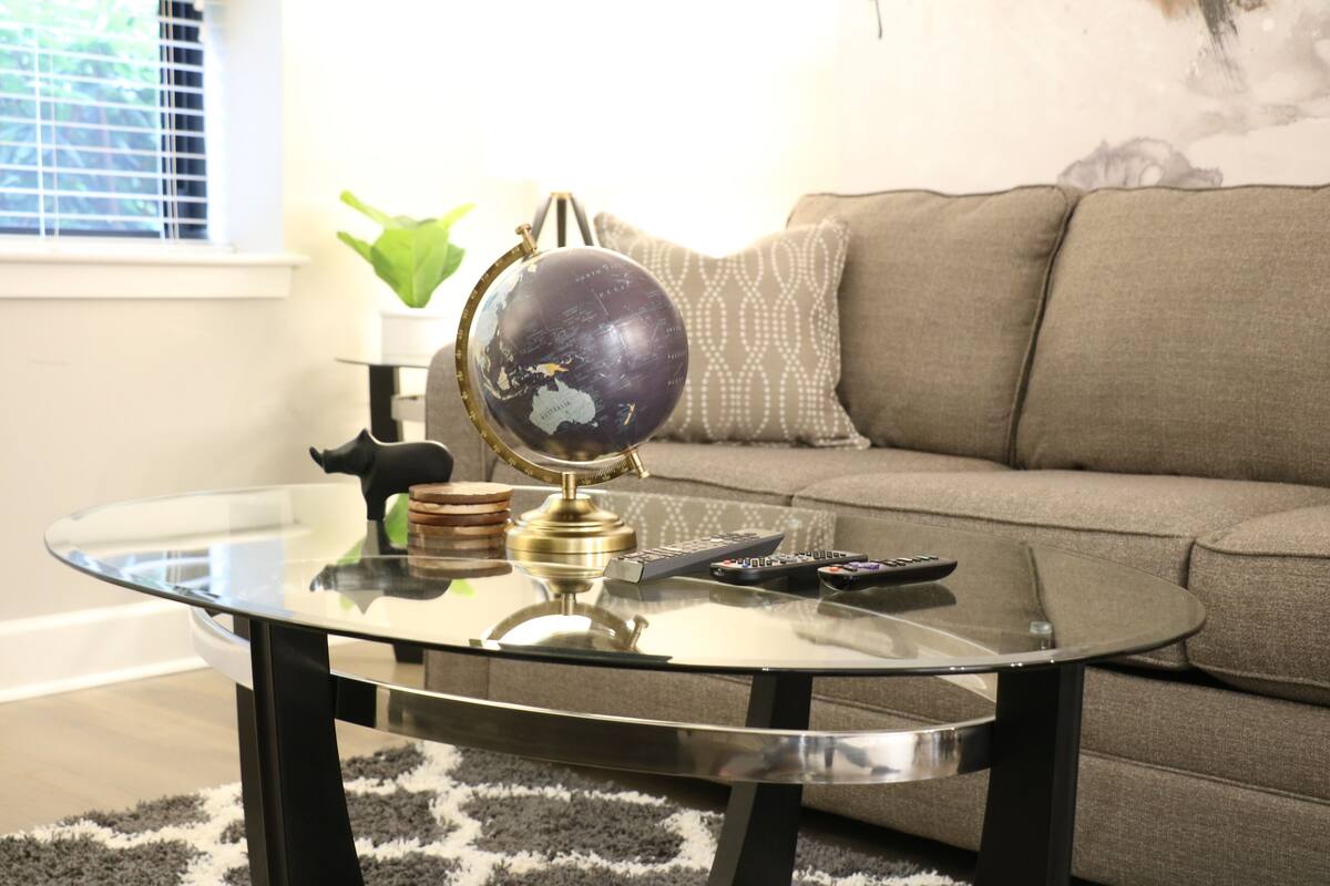 A living room with a glass coffee table, a globe, and a remote control.
