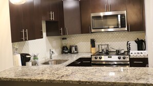 A modern kitchen with dark brown cabinets, a stainless steel microwave, a gas stove, and granite countertops. - Remarkable One Bedroom Suite (Boston)