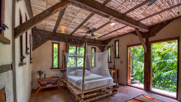 Una habitación con una cama, un banco de madera, una mesita pequeña y una alfombra colorida.
