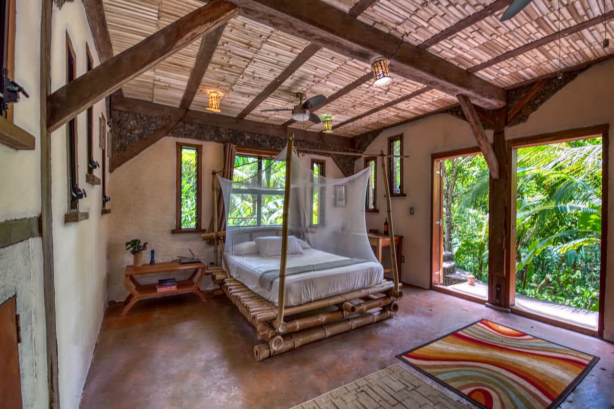 A room with a bed, a wooden bench, a small table, and a colorful rug.