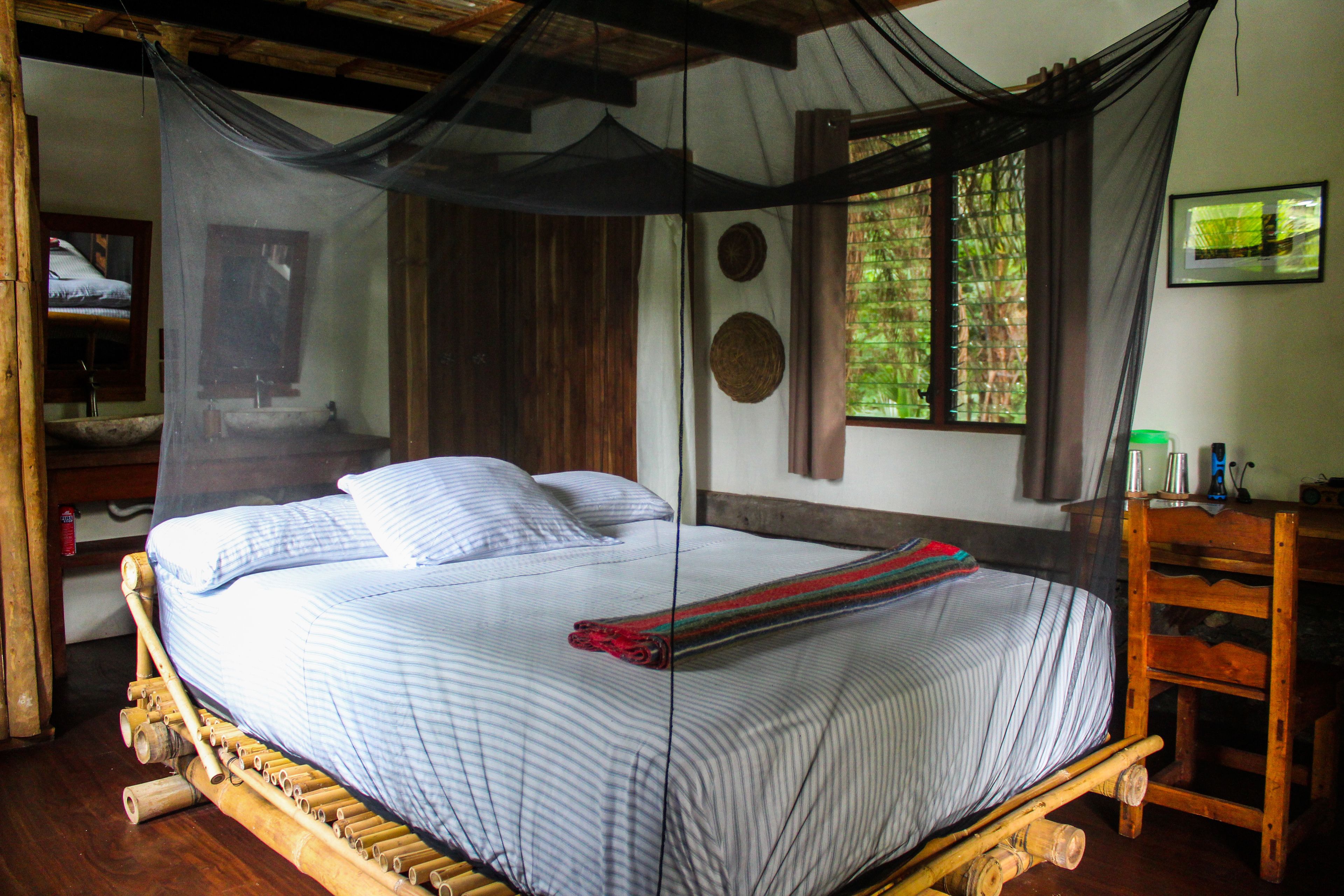 A bed with a mosquito net, wooden furniture, and a window with curtains.