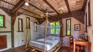 Una habitación rústica con una cama sostenida por bambú, un escritorio de madera y una pared de piedra.