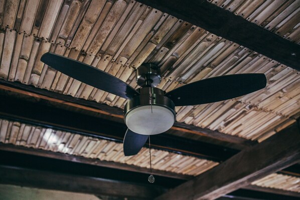 A ceiling fan with two blades, hanging from a wooden ceiling with a bamboo-like texture.