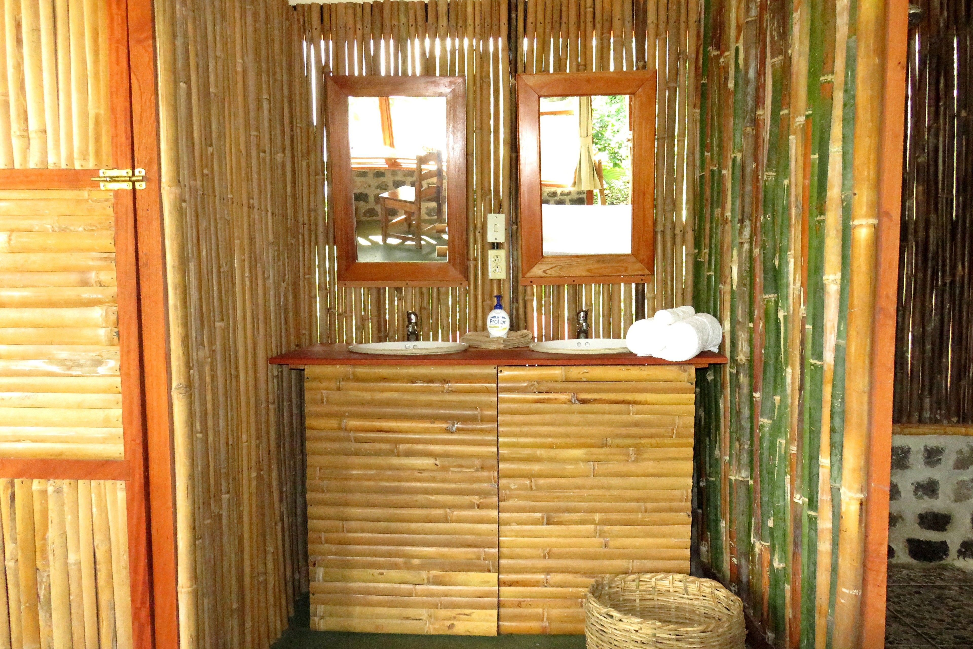 Un baño con motivos de bambú, que incluye dos lavamanos, un espejo y un cubo de basura pequeño.